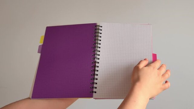 A hand flipping through colorful pages of a notebook with multi-colored dividers; minimalistic background.