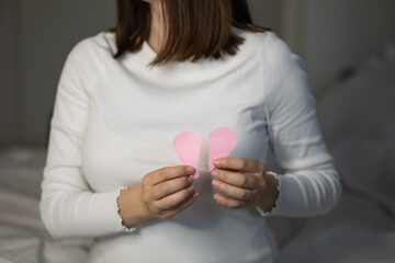 Woman sitting indoors, carefully holding two pink hearts in her hands. Concept broken heart valentine's day. breakup or divorce with husband. Family problems. Personal crisis