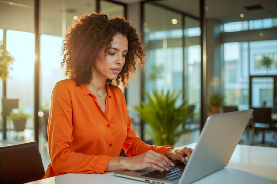 Woman in Orange Shirt Working on Laptop at Office Table