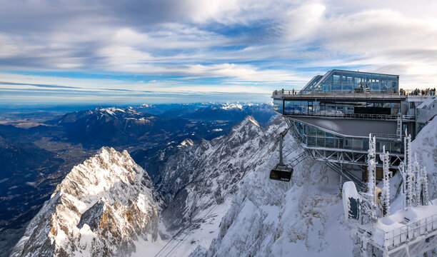 The Zugspitze near Garmisch-Partenkirchen (Bavaria) is the highest mountain in Germany. Panorama at the mountain station with cable car and view of the Alpine foothills on a sunny snowy December day.