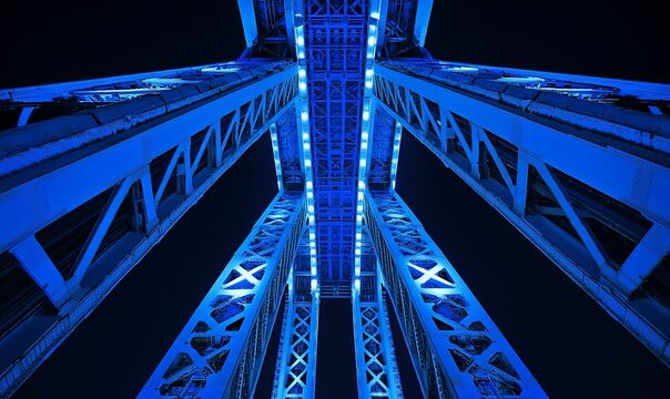 Blue illuminated bridge steel structure at night, low angle view, transportation infrastructure