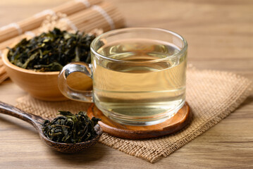 Hot green tea in cup glass and dried tea leaves in bowl with spoon on wooden background, Healthy drink