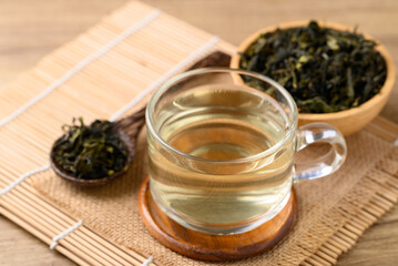 Hot green tea in cup glass and dried tea leaves in bowl with spoon on wooden background, Healthy drink