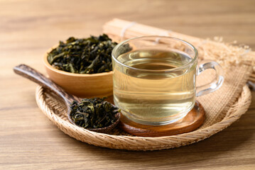 Hot green tea in cup glass and dried tea leaves in bowl with spoon on wooden background, Healthy drink
