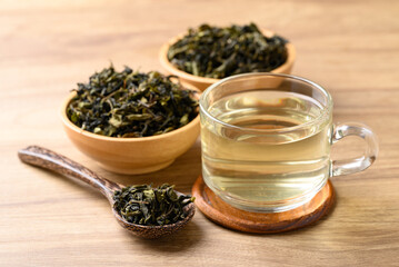 Hot green tea in cup glass and dried tea leaves in bowl with spoon on wooden background, Healthy drink