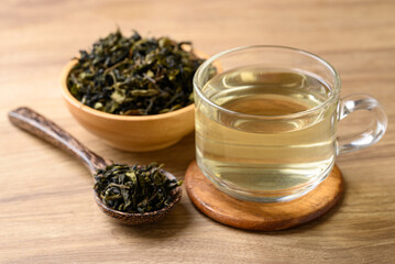Hot green tea in cup glass and dried tea leaves in bowl with spoon on wooden background, Healthy drink