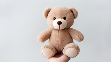 Obraz premium Soft teddy bear held by a hand against a simple gray background, perfect for gifts and decoration