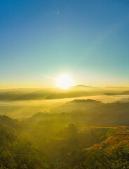 Aerial view of A breathtaking aerial view of a lush, green mountain range under a bright, clear blue sky, with sunlight illuminating the vast, rolling terrain and valleys below.