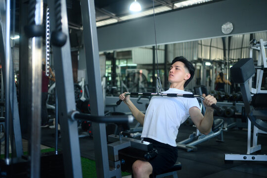 Athletic man working out on a lat pulldown machine in modern gym - Powered by Adobe