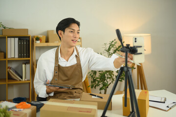 Young business owner adjusting smartphone on tripod for live streaming product sales online