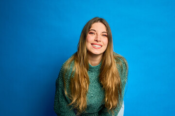 Young woman leaning forward and smiling on blue background