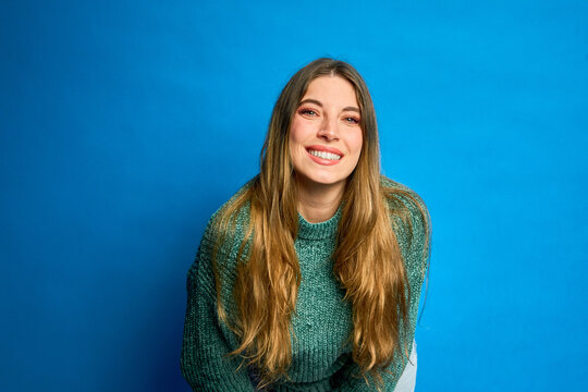 Young woman leaning forward and smiling on blue background