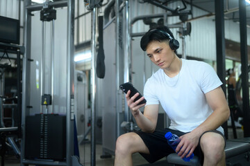 Young sportsman wearing headphones sitting on a gym bench and checking his phone
