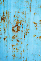 A close-up of a weathered blue metal surface with rust stains and peeling paint, creating an aged and distressed effect. The contrast between the faded blue and rusty orange tones adds a rustic feel