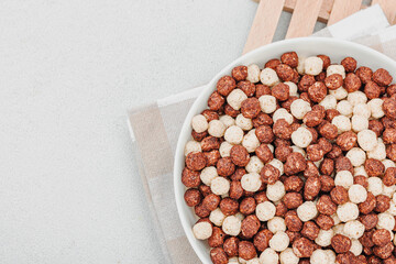 Vegan cereals in balls shape of cocoa and vanilla served with spoon. Full bowl ready to eat