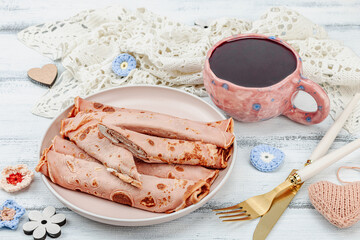 A cup of fragrant hibiscus tea and thin pancakes with cream. Good mood concept, cozy home comfort