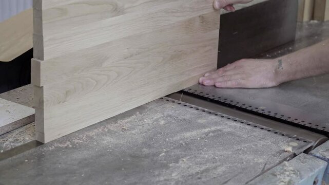 Carpenter uses a power jointer to cut the edges of wooden boards in a workshop. Focus on precision and craftsmanship in woodworking