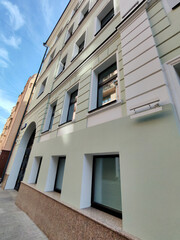 A modern light-colored building facade with large rectangular windows and a black arched entrance door. The image showcases clean urban architecture reflecting contemporary design trends