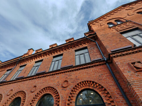 Close-up of a historic red brick building facade with arched windows and intricate masonry details. The perspective highlights the texture and craftsmanship of the exterior architecture. - Powered by Adobe