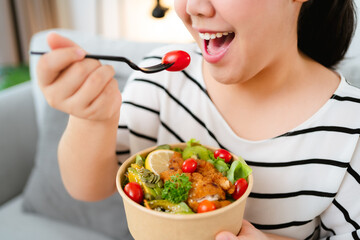 Beautiful plump woman holding a salad bowl and eating a salad in the bowl.