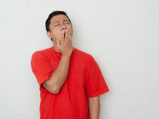 Young Asian man in a red shirt yawns with his hand over his mouth. Man in red shirt sleepy, healthy concept