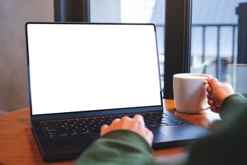 Fototapeta premium Mockup image of a woman typing on laptop computer with blank white desktop screen while drinking coffee in cafe