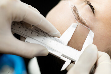 An unrecognizable beautician performs a microblading treatment on a girl's eyebrows in a beauty...
