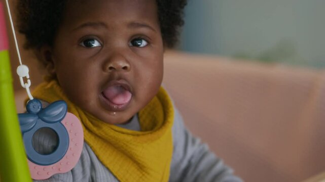 Close-up shot of curly-haired African American toddler in yellow bib looking around her nursery with open mouth
