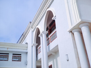 white mosque facade with intricate arched windows and balconies, reaching towards a clear blue sky
