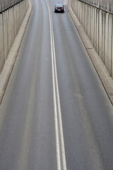 An asphalt road with a double white line exiting a underpass with a single car in the distance