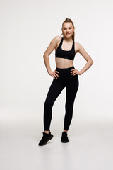 Obraz premium Confident sportswoman holding hands on waist, fitness trainer standing in power pose, workout in gym, white background
