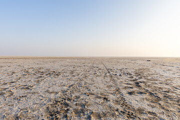 white salt flats desert with vehicle tire tracks leading line and bright blue sky at morning