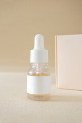 Glass bottle with facial serum and cardboard box on beige background, vertical. Minimal mockup skin care beauty product