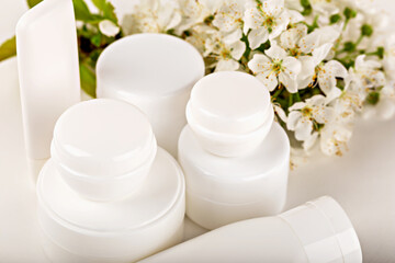 Mockup. White cosmetic containers displayed with blooming flowers, emphasizing beauty and elegance. Concept health and wellness, cosmetics and skincare. Various cosmetic containers on white background