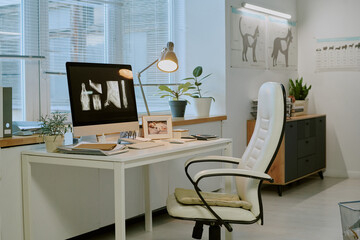 Veterinary office with an x-ray of animals displayed on a screen, modern white decor, and a comfortable chair. A pot plant and a lamp placed on the desk create an inviting atmosphere