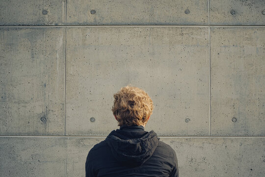 Back view of a person staring at a blank concrete wall