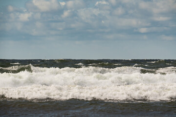 Wild beauty of the Baltic Sea: Powerful waves with white foam crash on the sandy shore of Estonia under a gray sky, creating a dramatic landscape.