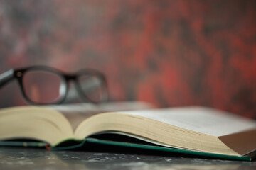 Open book lying on tabletop and glasses lying on book, red blurry wall in background. Space for text, design.