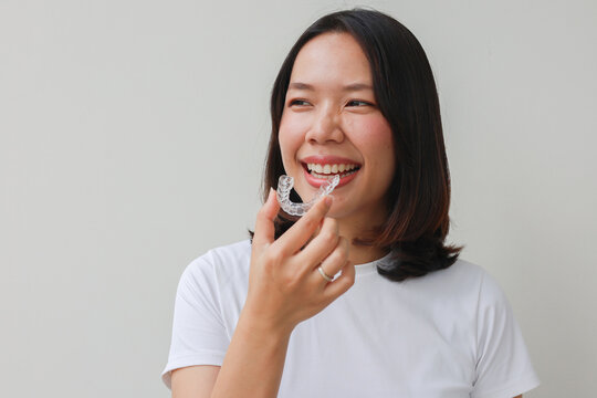 close up young asian beautiful woman smiling with hand holding dental aligner retainer (invisible) at dental clinic for beautiful teeth treatment course concept