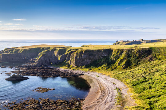 The cliffs and beach at Strathlethan Bay, near Stonehaven in Aberdeenshire, with Dunnottar Castle in the distance. Taken just after sunrise.