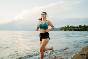 Young woman running or jogging on the beach at sunset	
