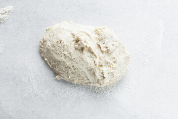 Overhead view of high hydration dough being shaped on a white granite countertop, top view of homemade bread dough on white countertop, process of making artisan bread