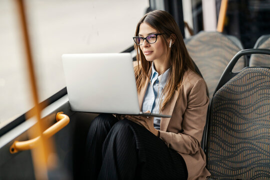 A young woman in suit sitting in city public bus and looking at laptop.
