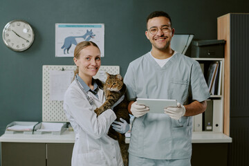 Portrait of veterinarians standing in clinic holding cat and smiling at camera, showing care and...