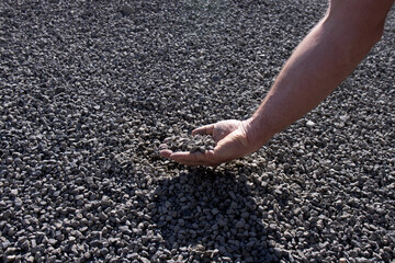 Gray gravel in man's hand against the background of the pile is illuminated by the sun