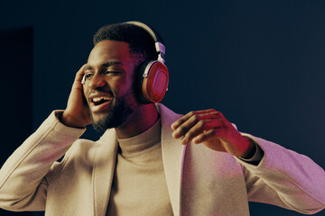 Young man enjoying music with headphones, smiling in a stylish coat, against a colorful background...