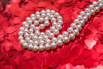 Pearl necklace on a background of red hearts
