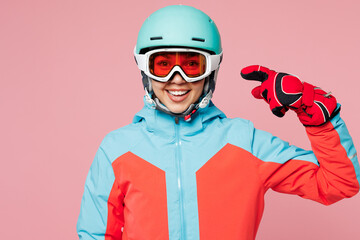 Snowboarder young woman wears warm blue padded jacket ski goggles mask point index finger on helmet spend extreme weekend winter season in mountains isolated on plain pink background. Hobby concept.
