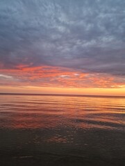 Serene ocean or sea at sunset, gentle waves, vibrant hues of orange, pink, and purple, dramatic sky, sense of romance, slowing down, tranquility, meditation, peacefulness