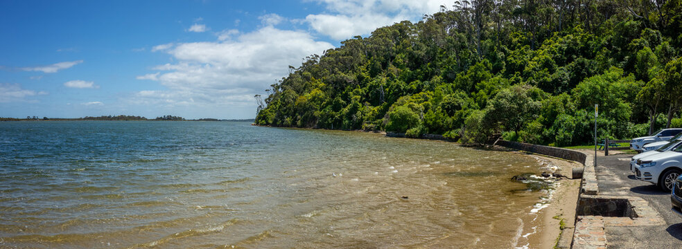 Panoramic view at a coastal car park with parked cars at Kalimna waterfront, overlooking the calm waters of Lakes Entrance. Kalimna Jetty Walk, VIC Australia.